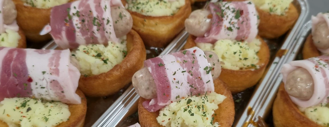 Yorkshire pudding portions topped with mashed potato and bacon-wrapped sausages, prepared by Homer Hill Butchers