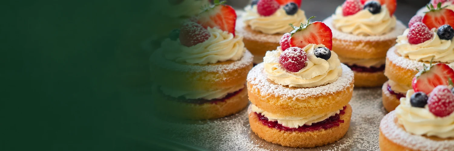 Victoria sponge cakes with jam, cream and berries, with a whole cake visible in the foreground